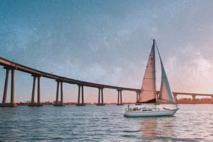 Evening Passage A sailboat passing beneath the Coronado Bridge in San Diego under a dramatic star-filled sky.
