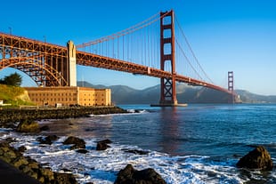 Golden Morning The Golden Gate Bridge illuminated by morning sunlight with waves breaking along the rocky shoreline in San Francisco, California.